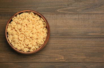 Raw dischi volanti pasta in bowl on wooden table, top view. Space for text