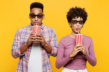 Young amazed surprised couple two friend family man woman wear purple casual clothes wear 3d glasses together watch movie film hold cup of soda pop in cinema look camera isolated on yellow background