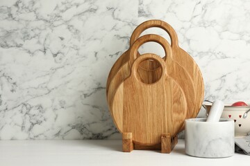 Wooden cutting boards and mortar with pestle on white table near marble wall, space for text
