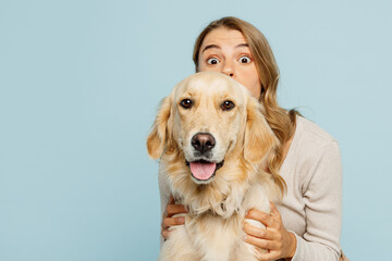 Young surprised shocked owner woman with her best friend retriever wear casual clothes look camera stand behind dog isolated on plain pastel light blue background studio. Take care about pet concept.