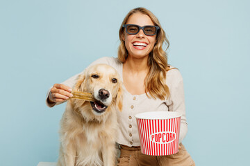 Young smiling owner woman with her best friend retriever wear casual clothes 3d glasses watch movie film hold bucket of popcorn in cinema feed dog give bone isolated on plain blue background studio.