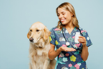 Young veterinarian woman wear uniform stethoscope heal exam retriever dog hold container with pills treatment isolated on plain pastel light blue background studio portrait. Pet health care concept.