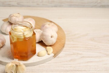 Honey with garlic in glass jar on light wooden table. Space for text