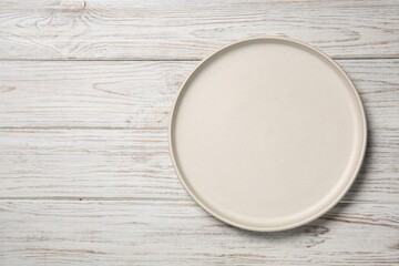 One white ceramic plate on light wooden table, top view. Space for text