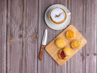 Scones are delicious with strawberry jam on a wooden tray and a coffee cup on a wooden table.