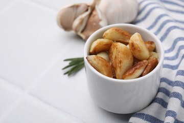 Fried garlic cloves in bowl on white table, closeup. Space for text