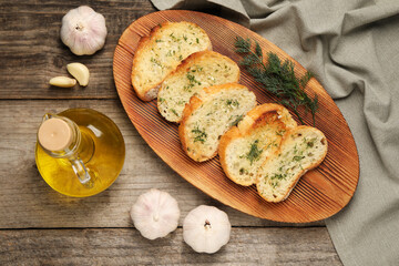 Tasty baguette with garlic, dill and oil on wooden table, flat lay