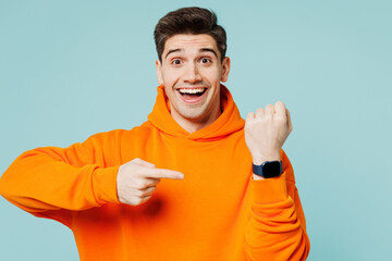 Young surprised shocked man wears orange hoody casual clothes show time point index finger on smart...