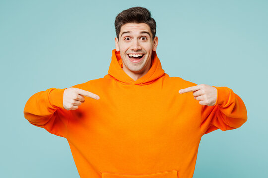 Young surprised man he wears orange hoody casual clothes point index on himself point index fingers on himself look camera isolated on plain pastel light blue cyan color background. Lifestyle concept.