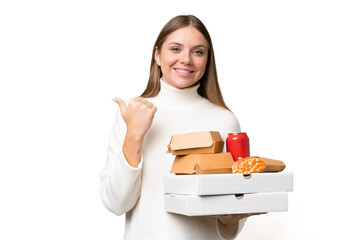 Young beautiful blonde woman holding takeaway food over isolated background pointing to the side to present a product