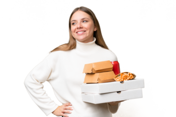Young beautiful blonde woman holding takeaway food over isolated background posing with arms at hip and smiling