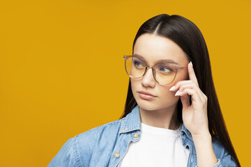 A beautiful girl in glasses poses on a yellow background