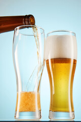Lager, ale flows to empty tall glasses from bottle.
