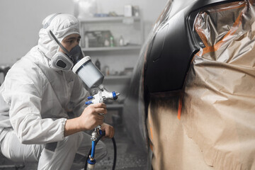 Male spray painter worker painting car body in paint booth. 