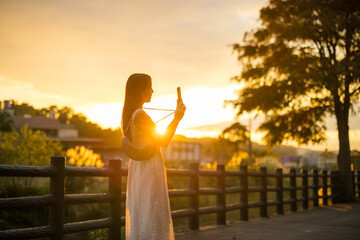 Woman use mobile phone to take photo under sunset - obrazy, fototapety, plakaty