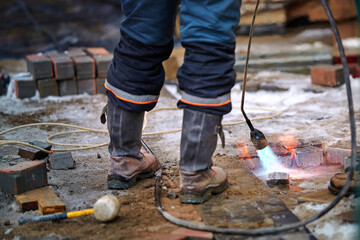 Worker dries wet surface with gas torch before paving work in winter season. Laying concrete paving...
