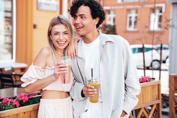Young smiling beautiful woman and her handsome boyfriend in casual summer clothes. Happy cheerful family. Female having fun. Couple posing in street. Holding and drinking cocktail drink in plastic cup