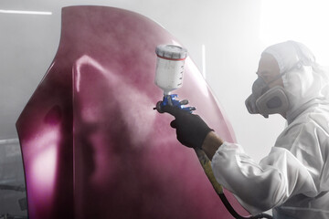 Professional spray painter worker applies finishing layer of varnish on purple car hood after main...