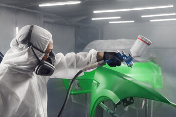 Car paint worker spraying green paint to car body element using spray gun in vehicle workshop chamber. Complex restoration of automobile body. 