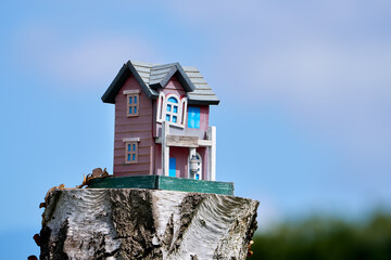 Buntes, verwittertes, kleines Holzhaus steht auf einem Baumstumpf vor blauem Himmel