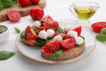 Delicious Caprese sandwiches with mozzarella, tomatoes, basil and pesto sauce on white wooden table