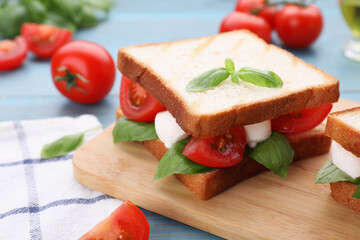 Delicious Caprese sandwich with mozzarella, tomatoes, basil and pesto sauce on light blue wooden table, closeup. Space for text