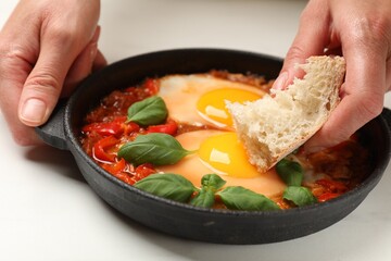 Woman dipping piece of bread into delicious Shakshuka at white table, closeup