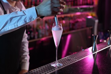 Bartender adding foam onto alcoholic cocktail at counter in bar, closeup