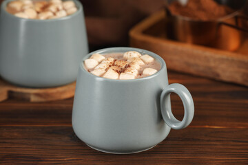 Cups of aromatic hot chocolate with marshmallows and cocoa powder on wooden table, closeup