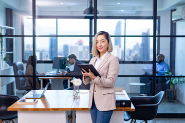 Portrait of Asian business CEO woman is standing in the office at the table with digital tablet and...