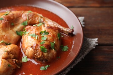 Tasty cooked rabbit meat with sauce and parsley on wooden table, closeup