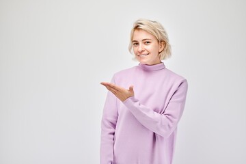 Young blond woman in casual holding something in hand, demonstrating empty space for product or...