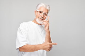 Gray-haired mature man 60 years old in white T-shirt pointing aside finger, demonstrating empty...