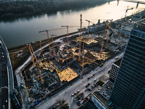 Top view of construction site with cranes in city, by river. Areal photography, modern municipal or urban engineering.