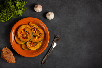 Delicious baked pumpkin on a brown plate, garlic, bread and spices, top vew. The concept of healthy vegetable dishes. The concept of Thanksgiving. Space for text 