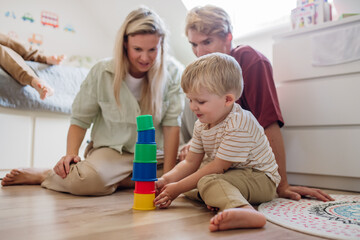 Parents looking at little boy building a tower in childrens room. Stacking blocks, building game...