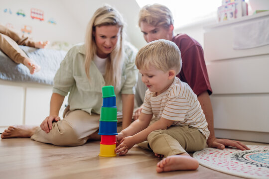 Parents looking at little boy building a tower in childrens room. Stacking blocks, building game for preschooler.