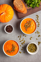 Pumpkin soup with seeds, spices, pepper and bread on a gray background, shot from above. The...