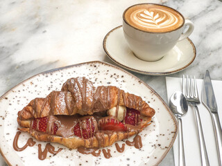 delicious croissant with strawberry fruit and chocolate by cup of cappuccino