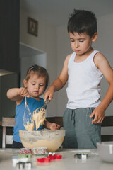 Brother and sister mixing flour and water to create dough for cupcakes. Children helping parents.