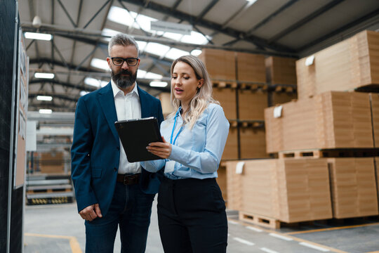 Female engineer and male production manager standing in modern industrial factory, talking about production. Manufacturing facility with robotics and automation.