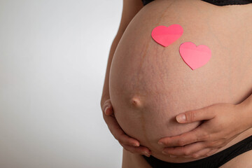 Pregnant girl with a big belly and pink hearts on a white background. The concept of love and motherhood for future children. Copy space for text. Preparation for childbirth