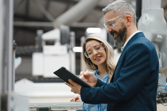 Female engineer and male production manager standing in modern industrial factory, talking about production. Manufacturing facility with robotics and automation. - Powered by Adobe