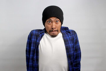 A worried young Asian student, dressed in a beanie hat and casual shirt, appears anxious and fearful about facing a challenging question during the final exam. Standing against white background.