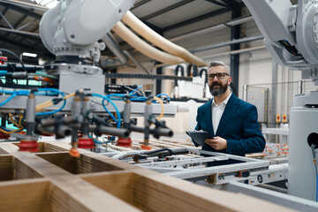 Male engineer in modern industrial factory, checking robotic arm, controling process and...