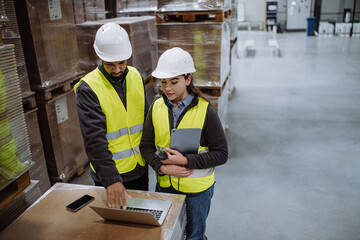 Warehouse manager talking with logistics employee in warehouse, planning transport of products,...