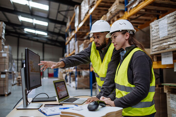 Warehouse manager talking with logistics employee in warehouse, planning transport of products,...