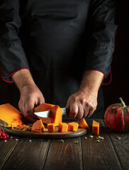 A chef prepares pumpkin porridge with his hands in a restaurant kitchen. Working medium on the kitchen table with spices and pieces of chopped pumpkin.