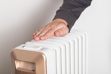 A man's hand against the background of an electric heater radiator on a white background. Concept...