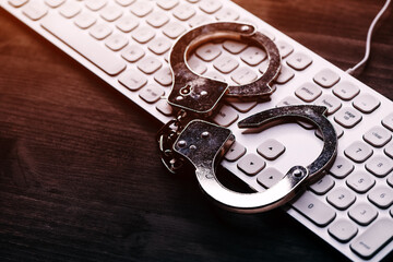 High tech IT cyber crime arrest concept, image of police handcuffs over computer keyboard